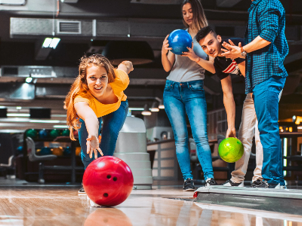 girl bowling with a red ball whilst friends look on and cheer