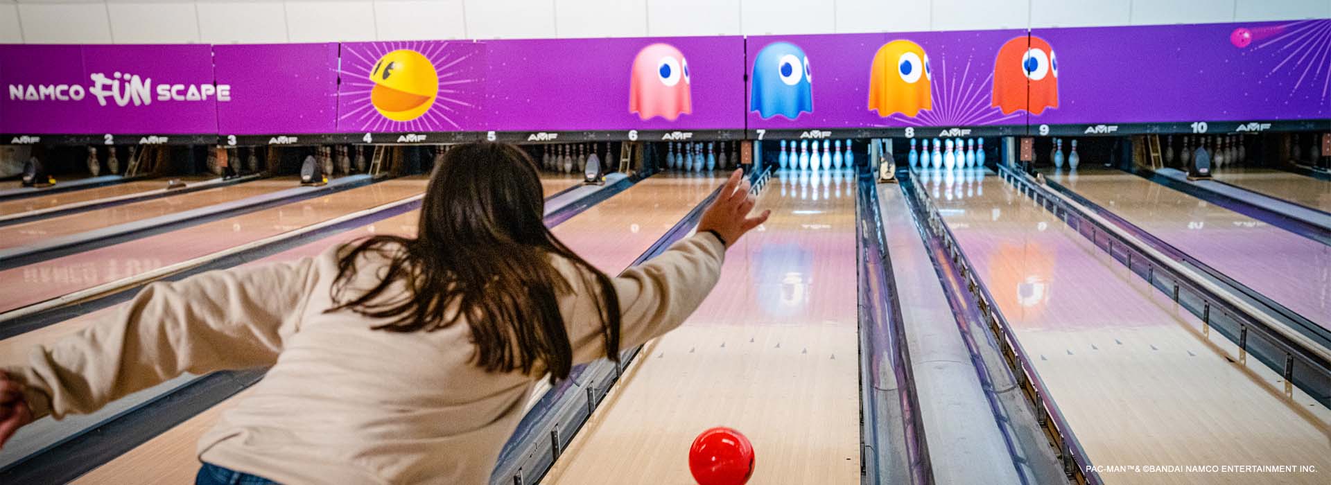 Woman throwing a red bowling bowl down a bowling lane at namco funscape