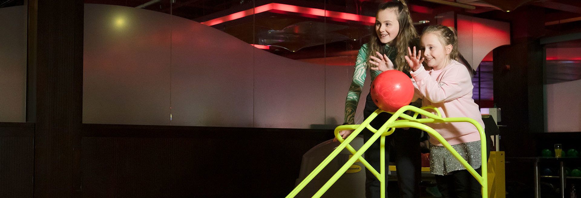 Sisters pushing bowling ball down a ramp