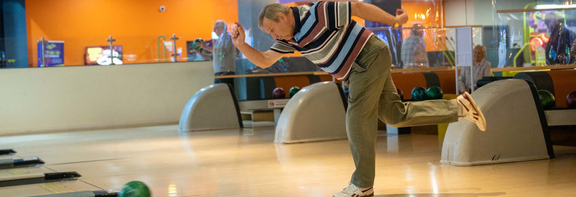 Old male throwing bowling ball down a bowling lane at namco funscape 