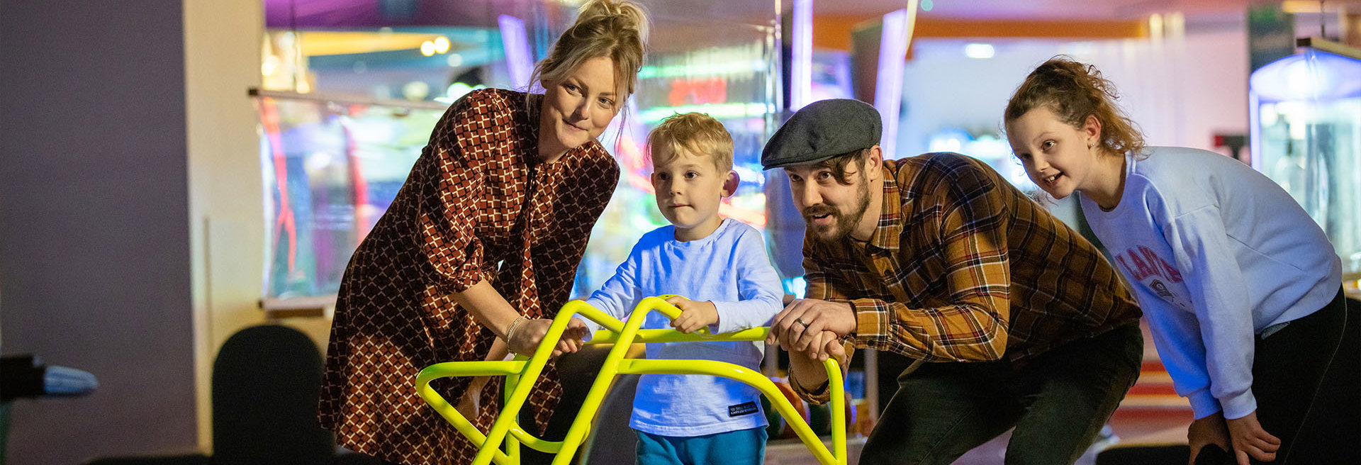 family encourage and help young child bowl using the bowling ramp at namco funscape